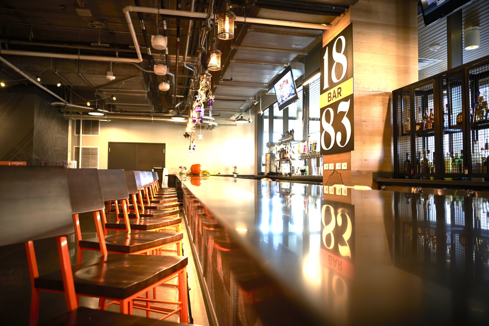 Modern bar interior featuring sleek, shiny counter and colorful illuminated decor. Empty chairs line the counter, showcasing the bar's inviting atmosphere.