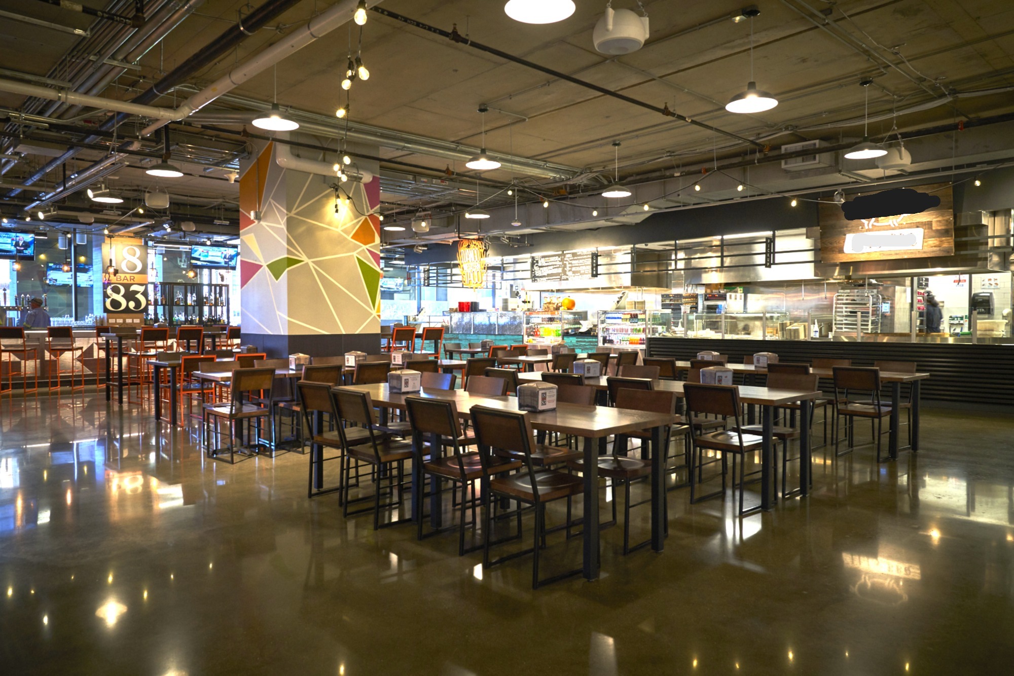 Modern dining area with wooden tables and chairs, featuring a vibrant mural and an open kitchen behind. Ideal for casual meals.