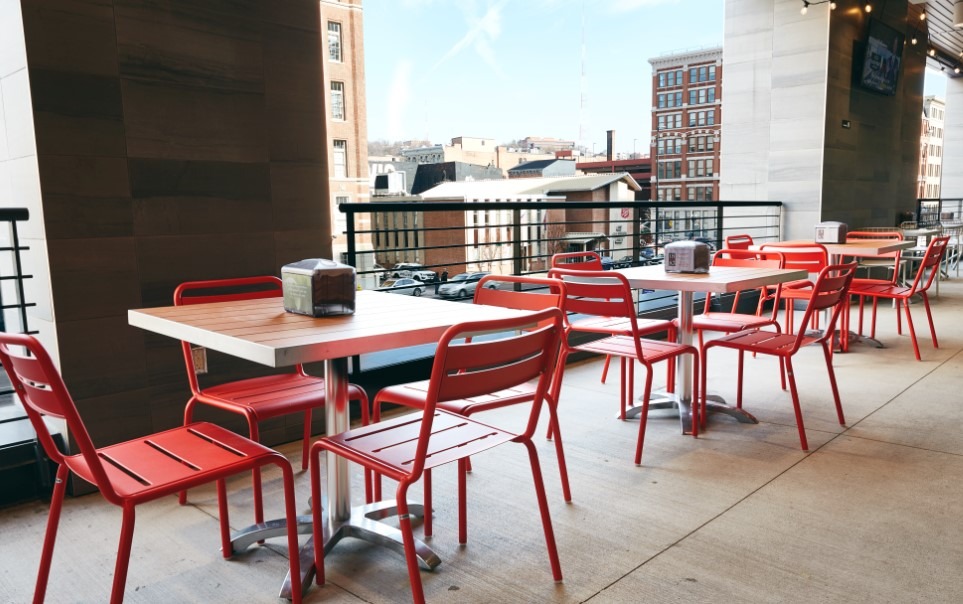 Bright outdoor dining area featuring red chairs and tables, perfect for social gatherings. Set against a cityscape background.