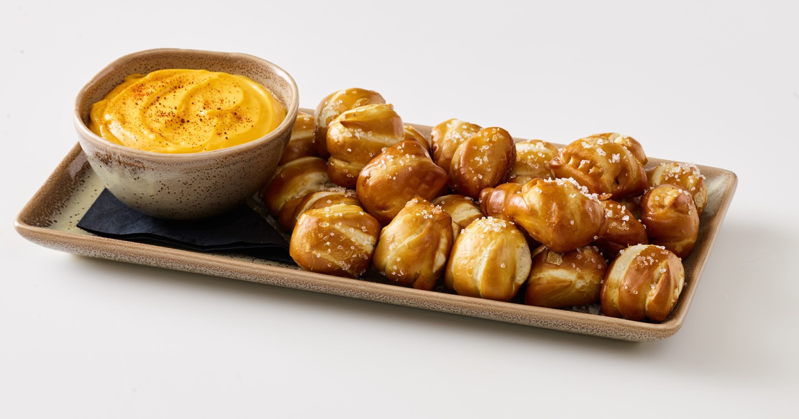 Soft pretzel bites sprinkled with coarse salt, served with a creamy cheese dip in an earthy bowl, ideal for sharing or snacking.