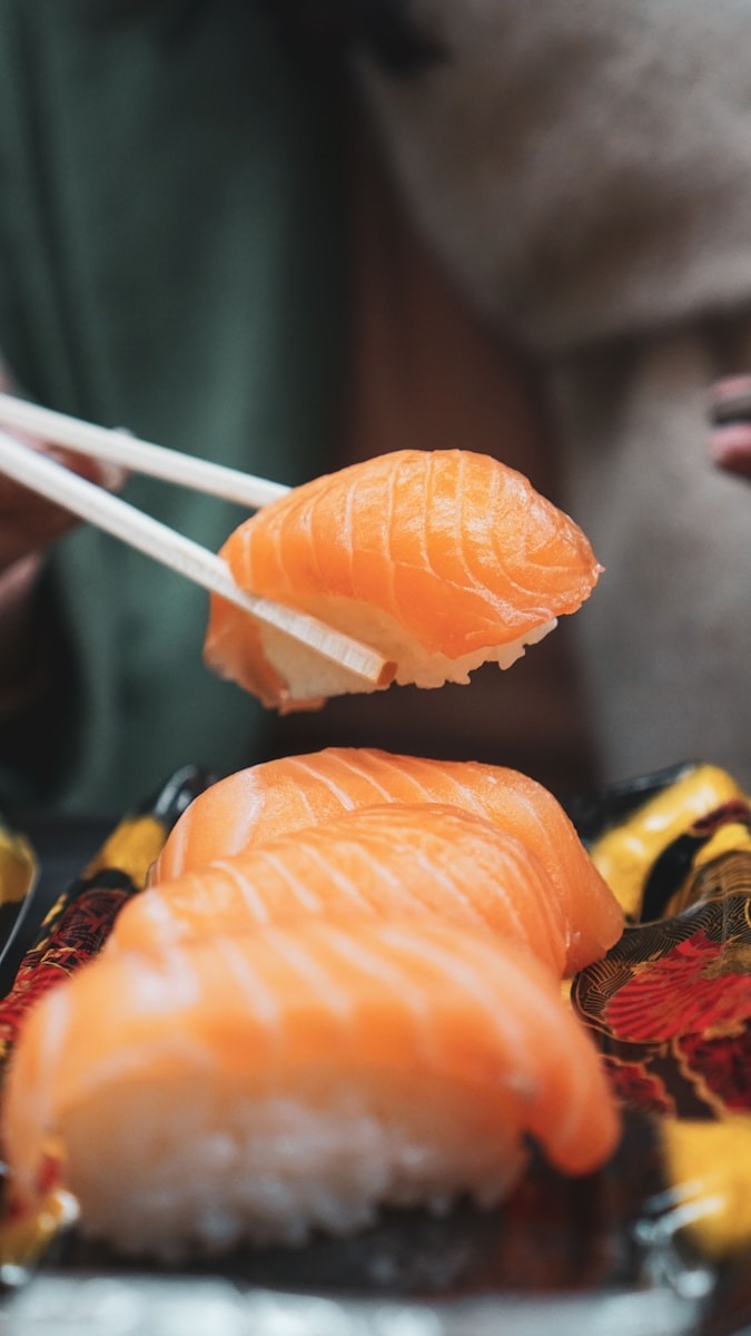 Salmon sushi being picked up with chopsticks, showcasing vibrant orange slices on rice, emphasizing the dish's appeal and cultural significance.