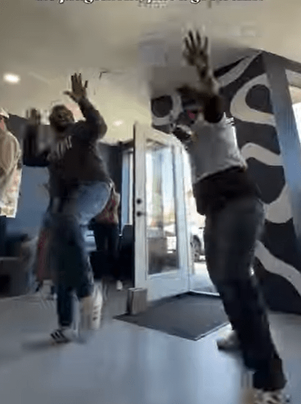 Two people joyfully dancing in a brightly lit entrance with a patterned wall, showcasing a lively atmosphere and celebration.